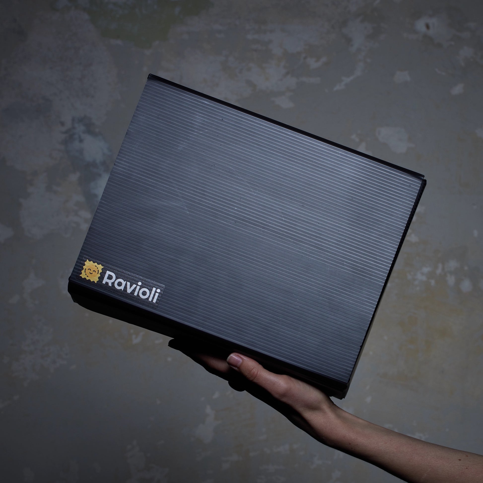 Foto einer schwarzen Ravioli-Verpackung von der Seite. Sie wird von einer Hand gehalten und das Ravioli Logo ist sichtbar.