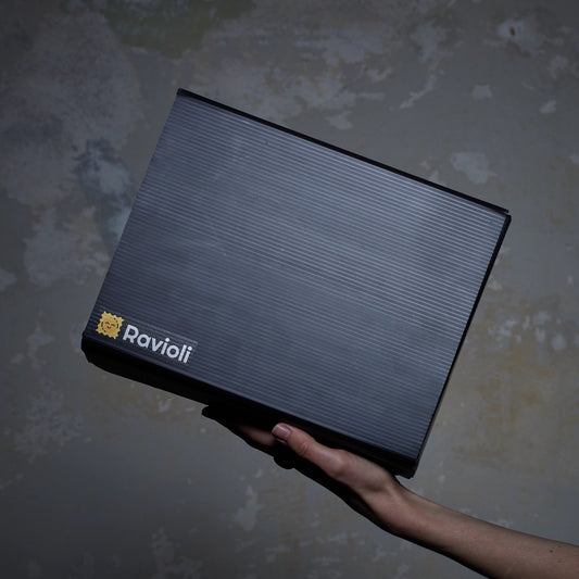 Foto einer schwarzen Ravioli-Verpackung von der Seite. Sie wird von einer Hand gehalten und das Ravioli Logo ist sichtbar.